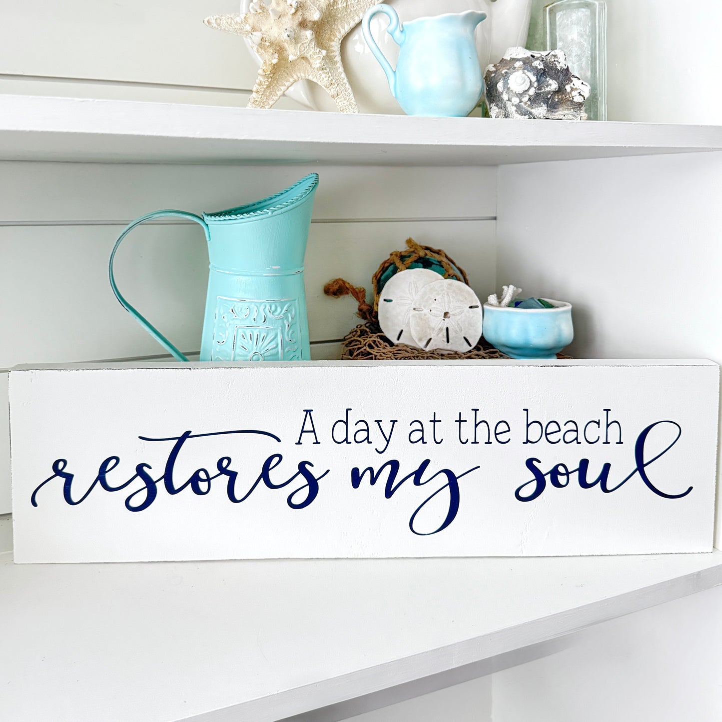Decorative shelf with beach-themed items and a sign reading 'A day at the beach restores my soul'.