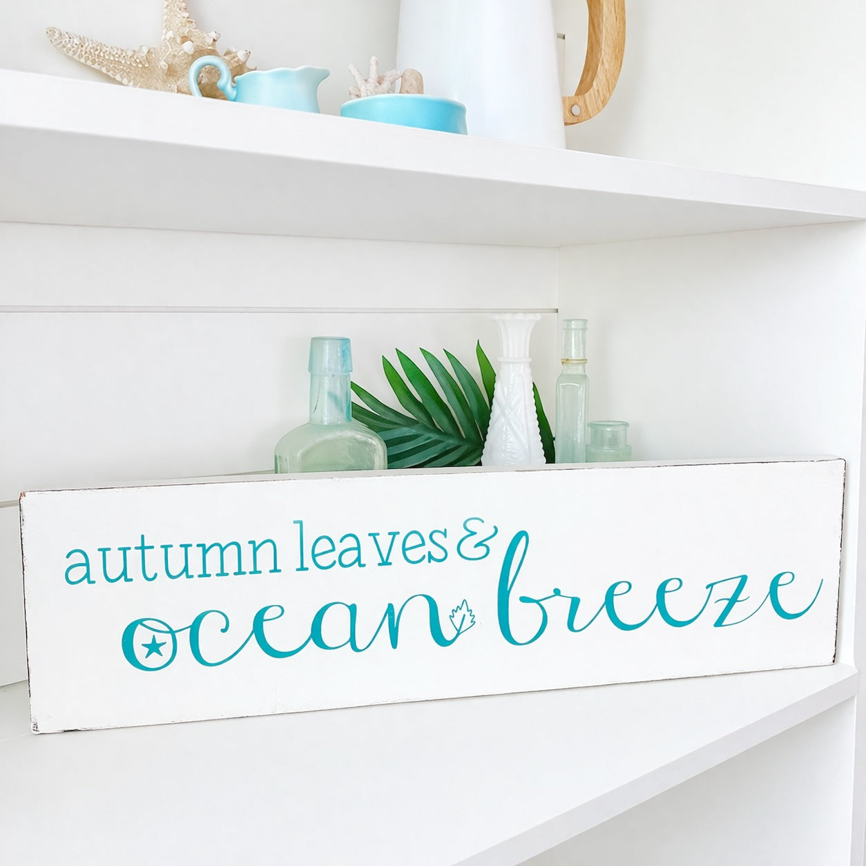 Decorative sign with 'autumn leaves & ocean breeze' text on a white shelf.