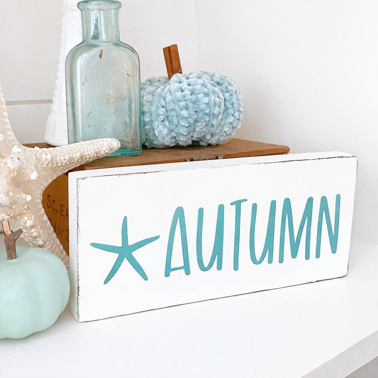 Decorative sign with 'AUTUMN' text and a starfish on a shelf with decorative items.