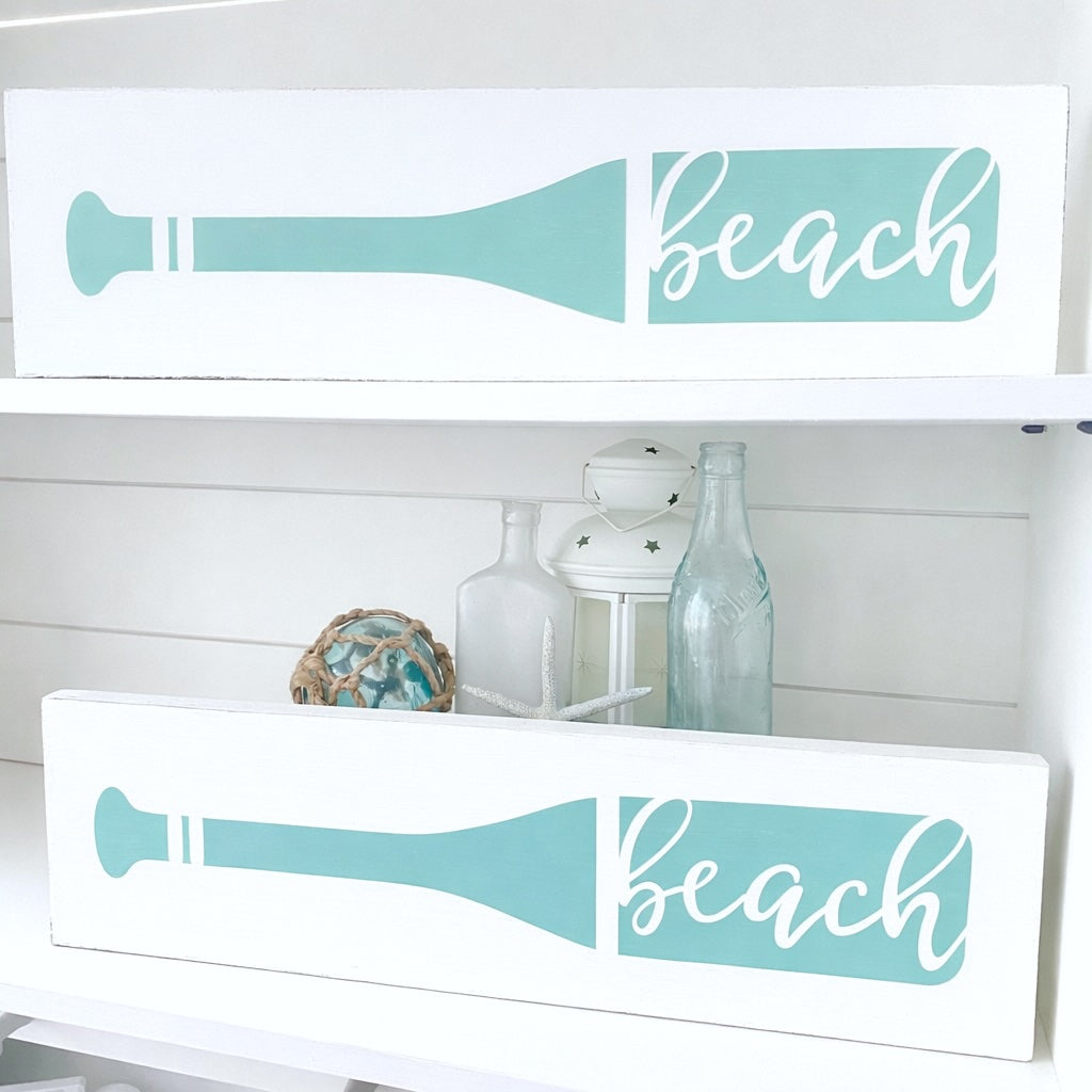 Decorative signs with 'beach' text and oar design on a white shelf.