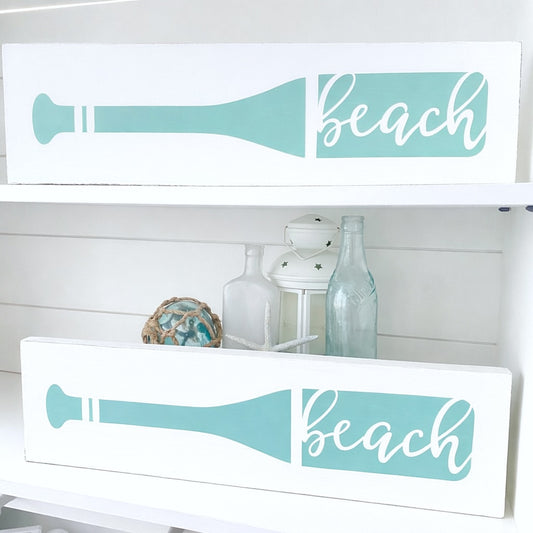 Decorative signs with 'beach' text and oar design on a white shelf.