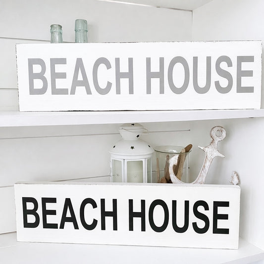 Two 'Beach House' signs on a shelf with decorative items.