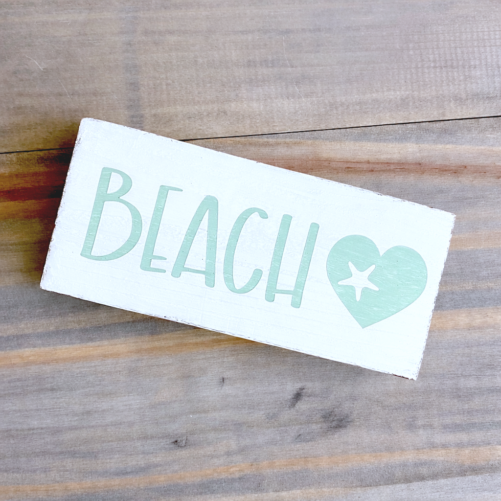 Decal with 'BEACH' text and heart design on a wooden surface