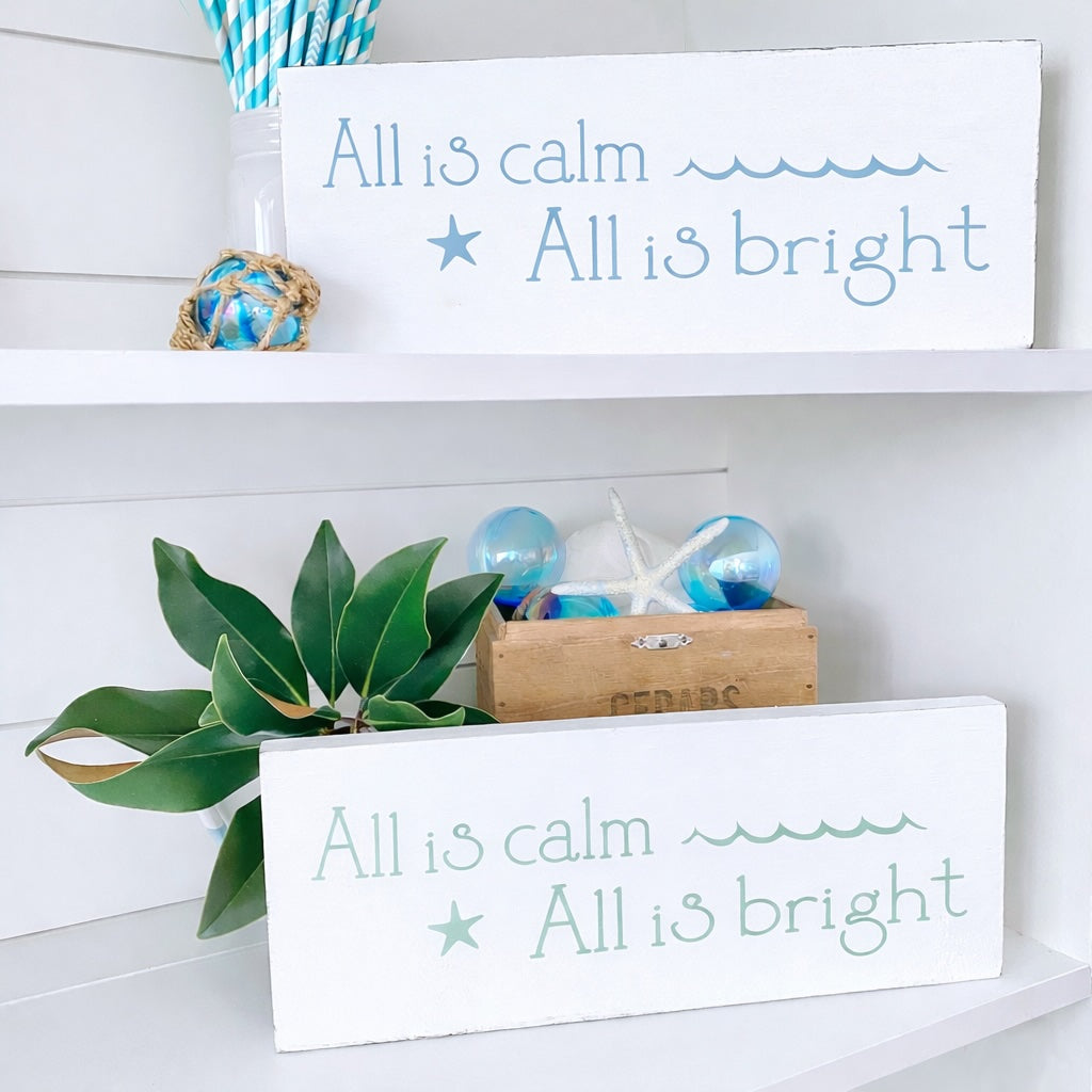Decorative signs with 'All is calm, All is bright' text on a shelf with plants and decor items.