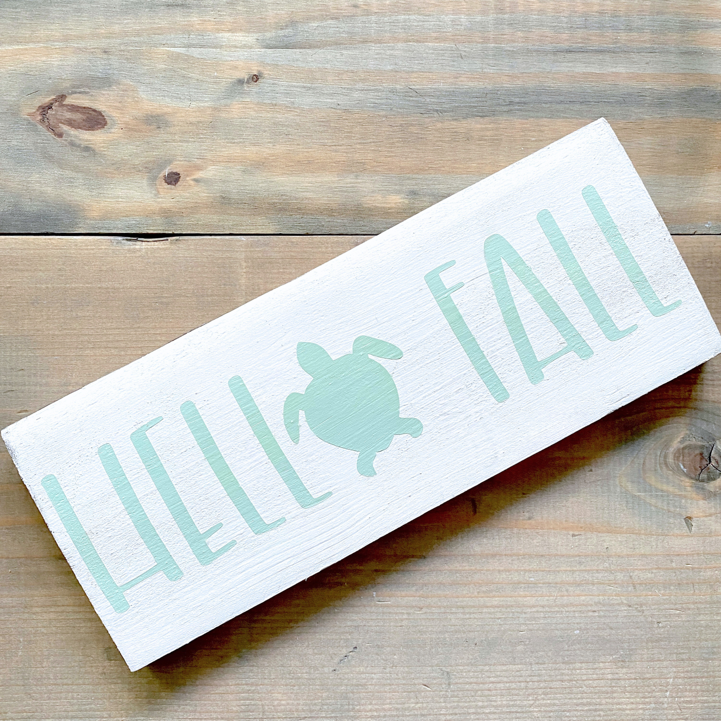Wooden sign with 'HELLO FALL' and turtle on a wooden surface