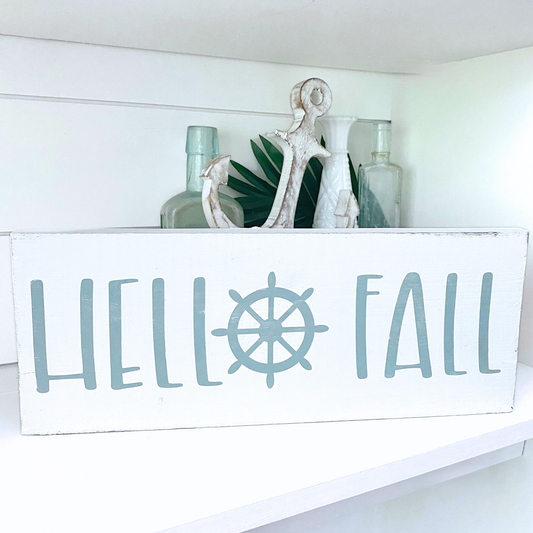 Decorative sign with 'Hello Fall' text and a ship wheel on a shelf.
