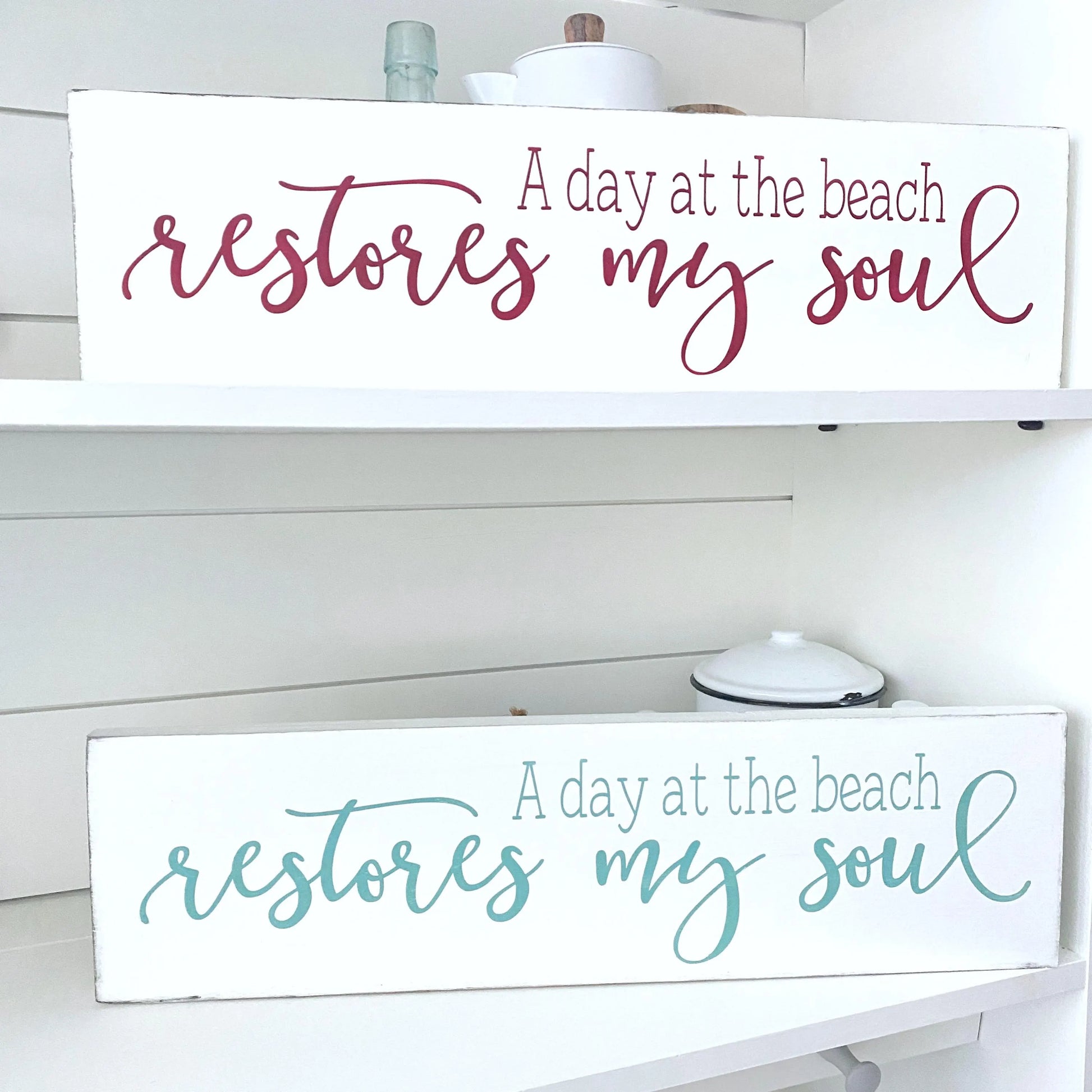Wooden signs with 'A day at the beach restores my soul' text on a white shelf.