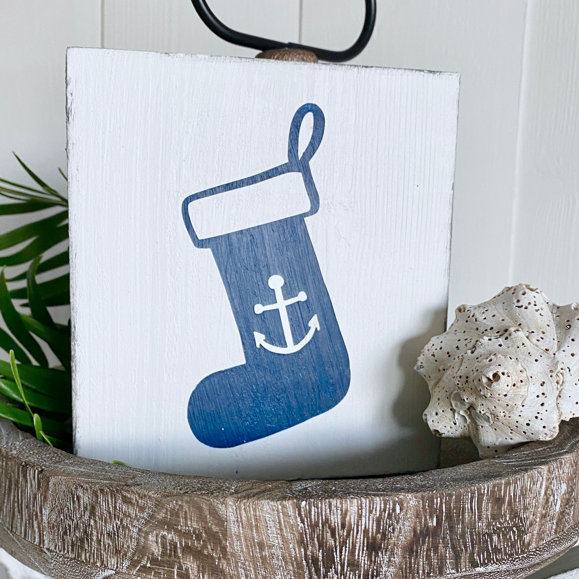 Decorative sign with a blue stocking featuring an anchor on a white background, placed in a wooden bowl.