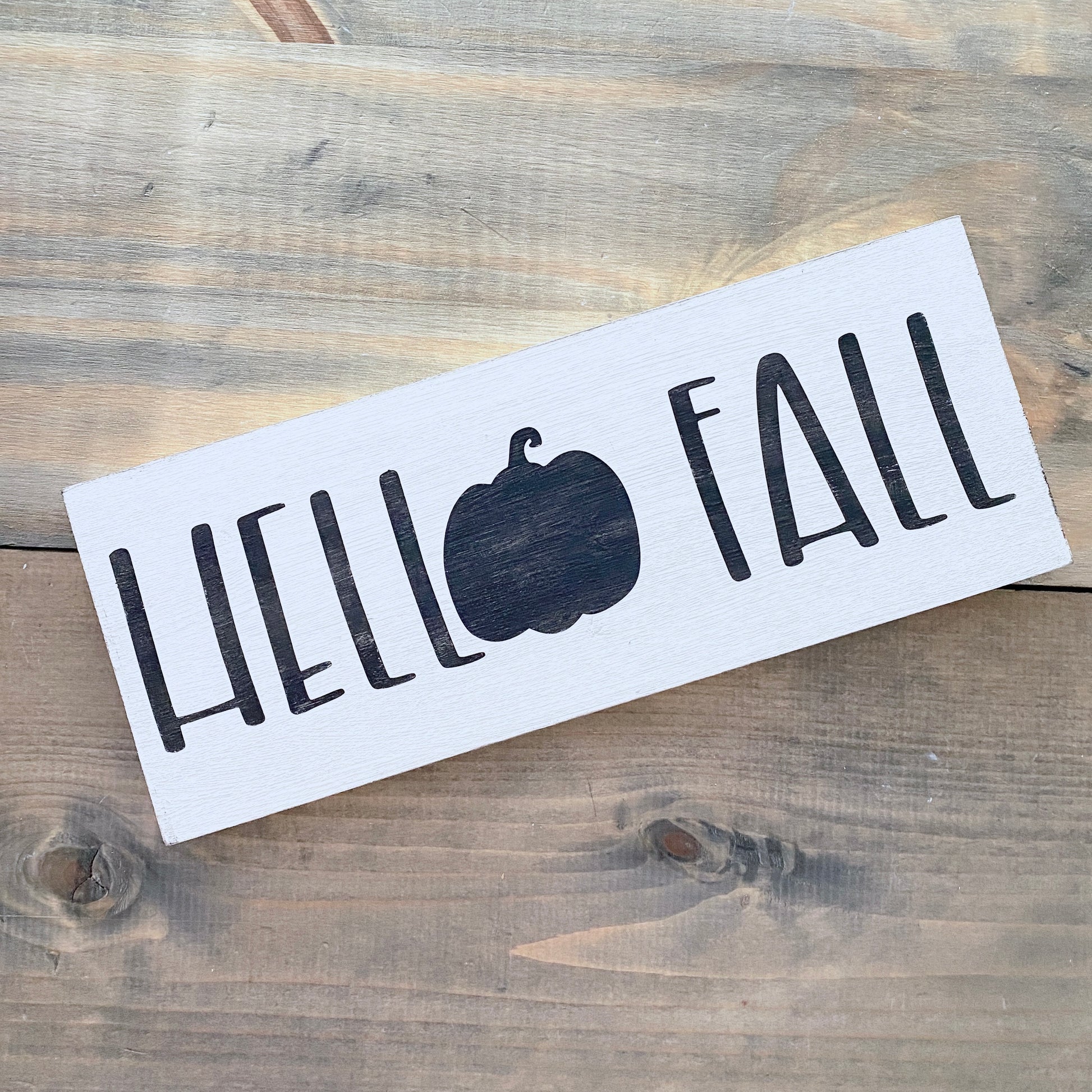 White sign with 'Hello Fall' and a pumpkin on a wooden surface