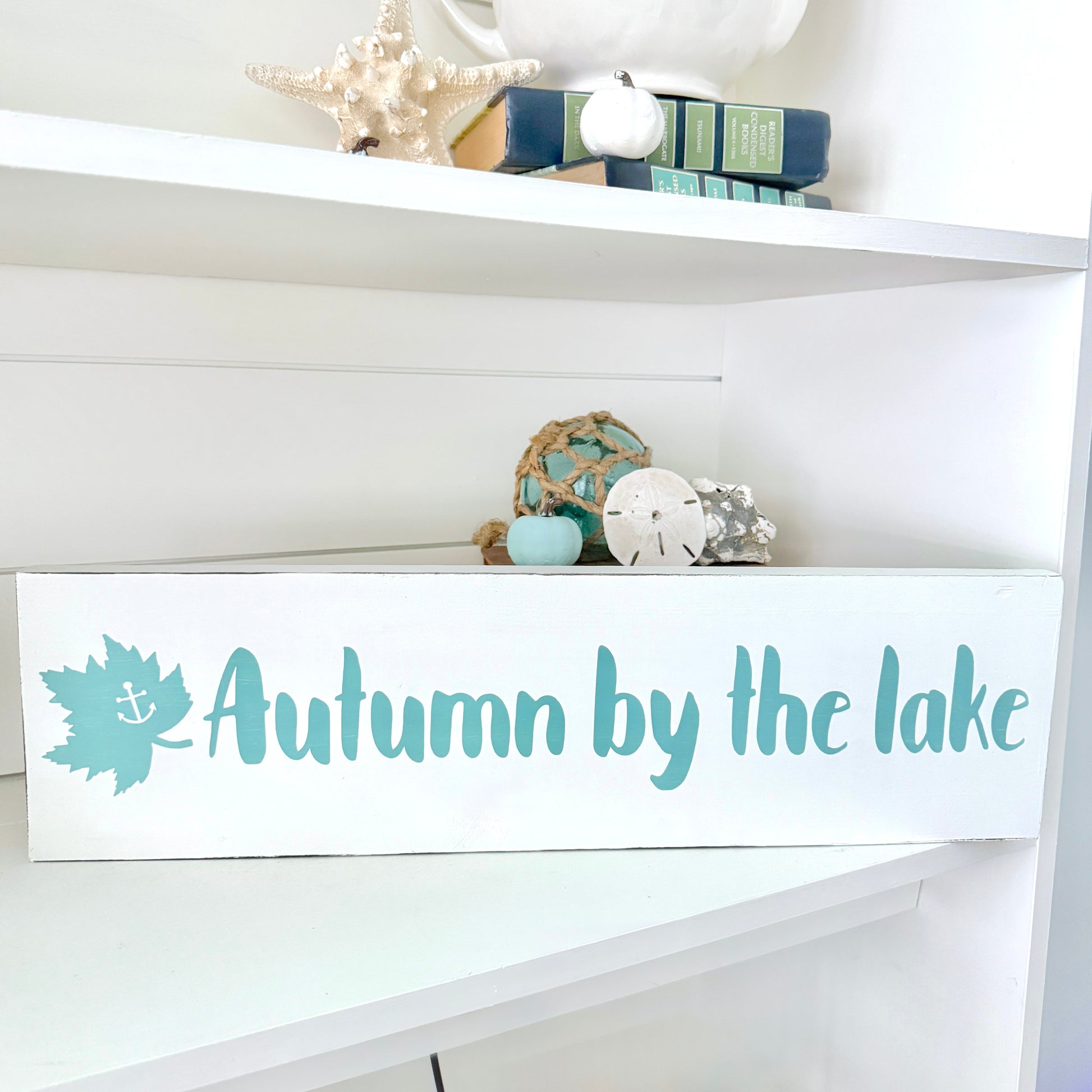 Decorative sign with 'Autumn by the lake' text on a shelf with decorative items.