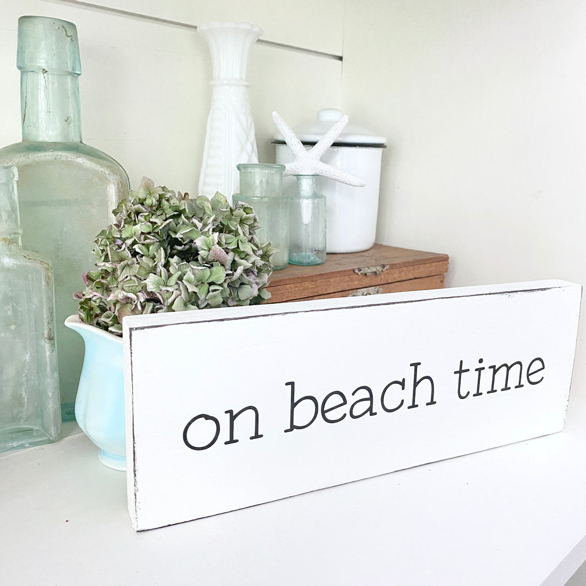 Decorative sign with 'on beach time' text on a shelf with decorative items.