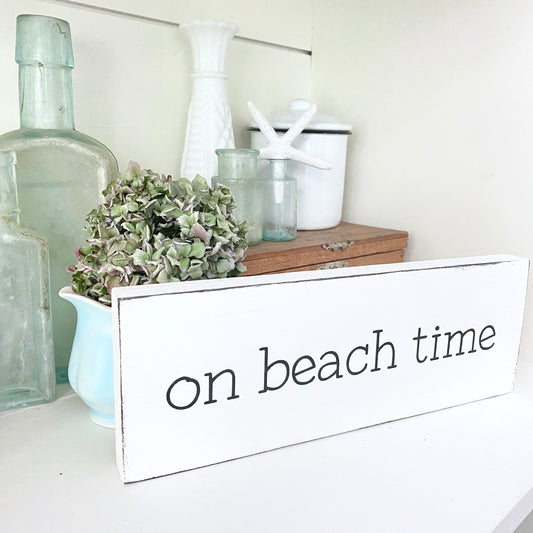 Decorative sign with 'on beach time' text on a shelf with decorative items.