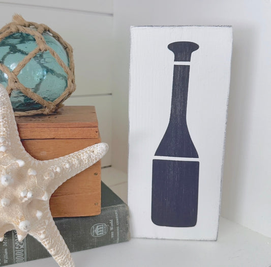 Decorative sign with an oar design next to a starfish and books on a shelf.