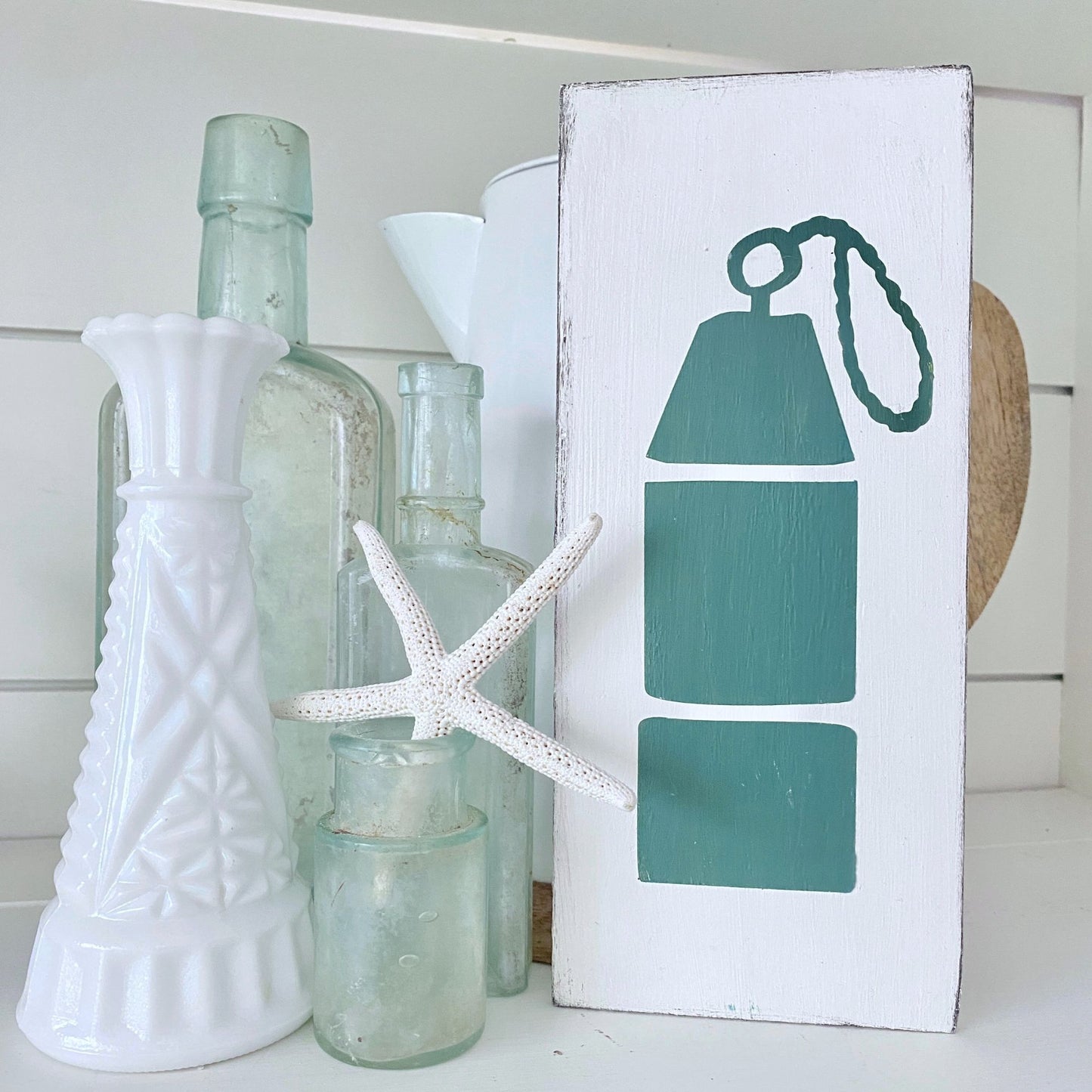 Decorative shelf with bottles, a starfish, and a sign with a buoy design.