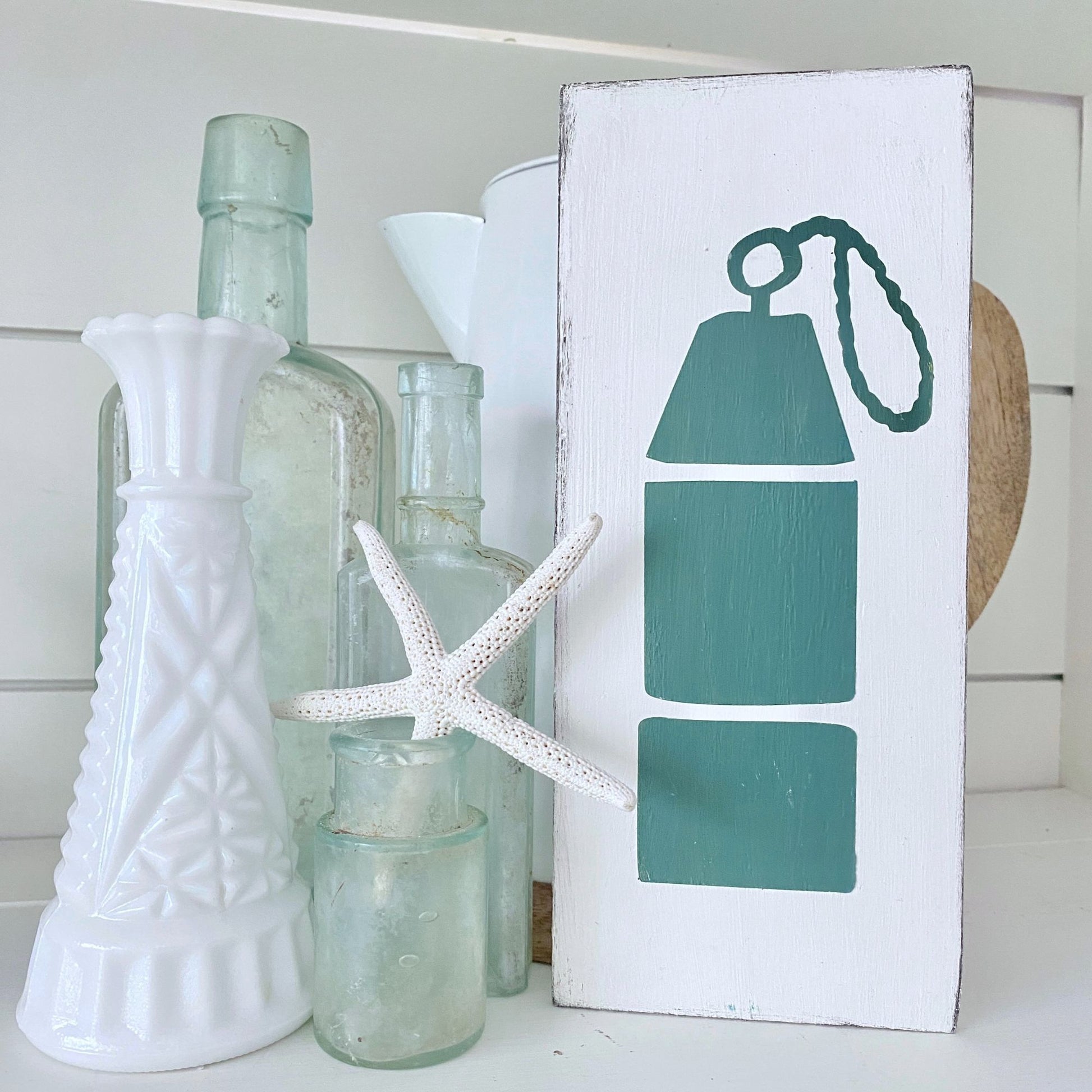 Decorative shelf with bottles, a starfish, and a sign with a buoy design.