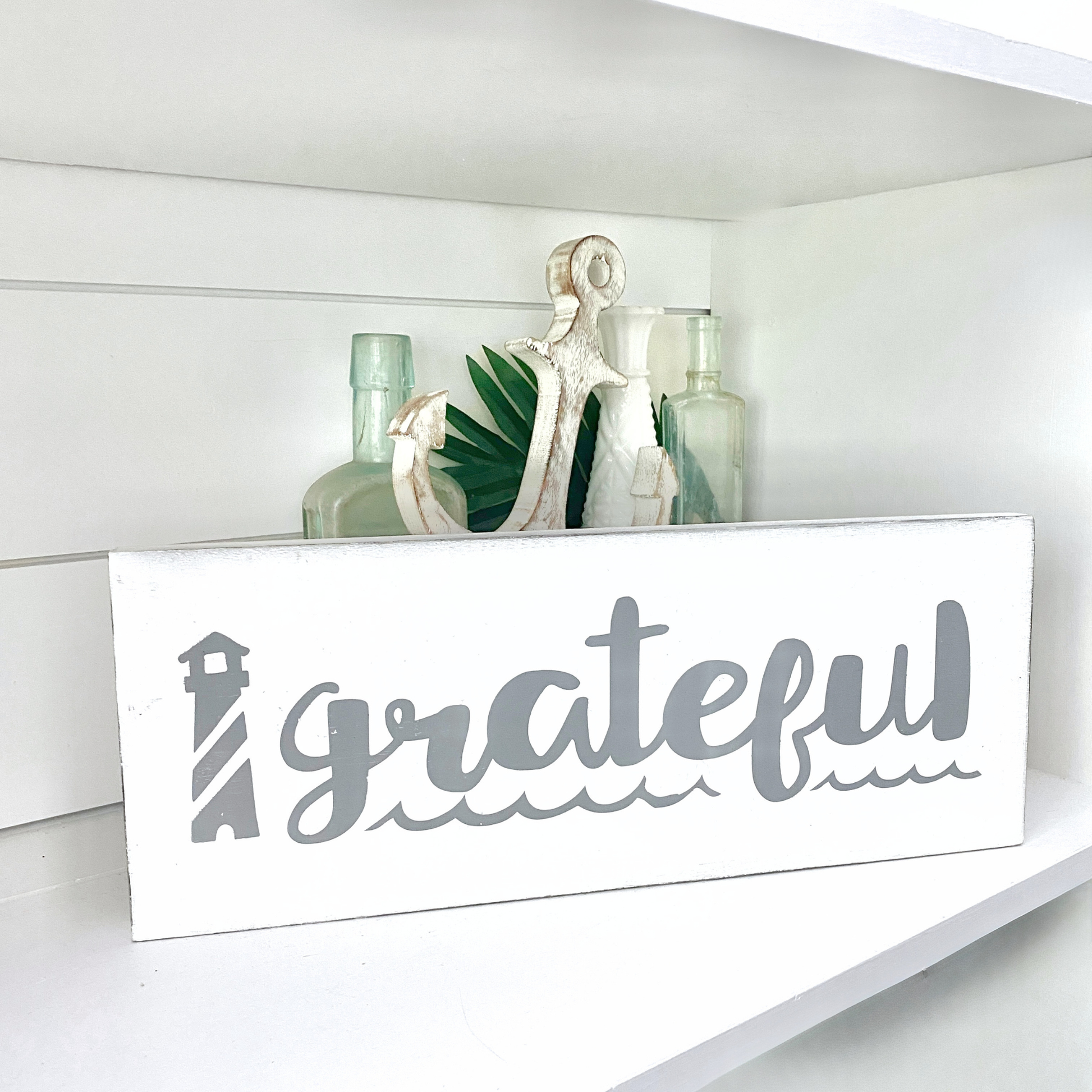 Decorative sign with 'grateful' on a shelf with plants and bottles.