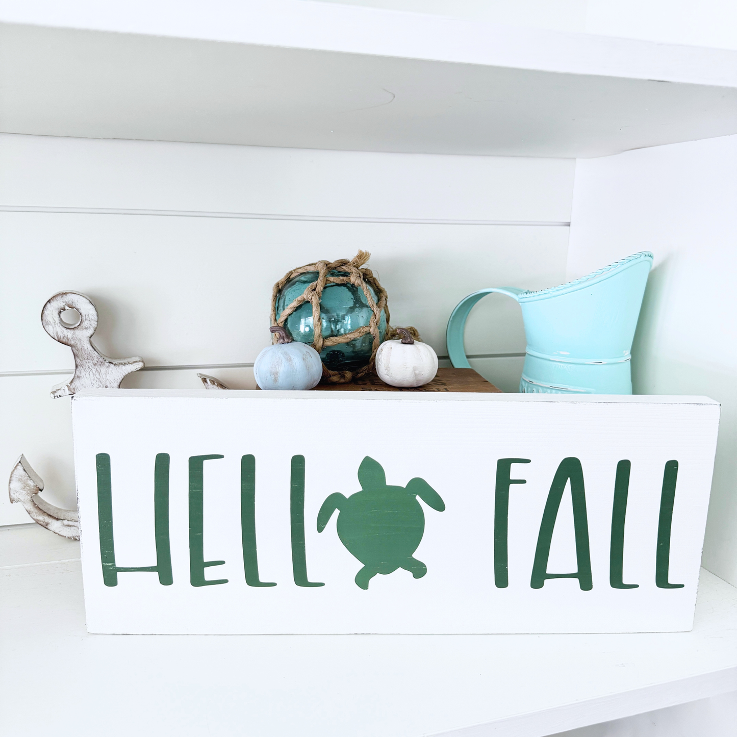 Decorative sign with 'Hello Fall' and turtle design on a white shelf.