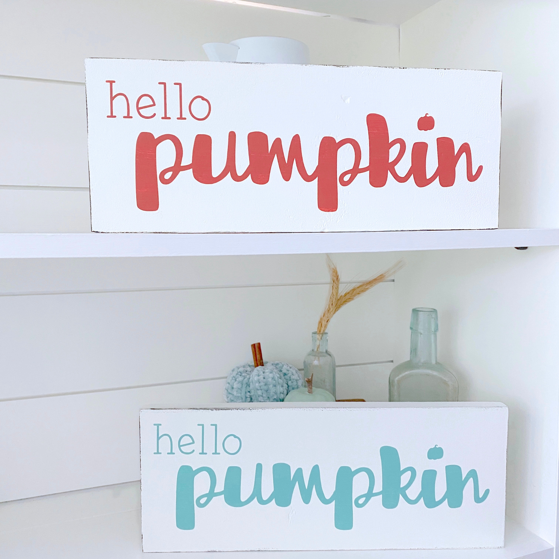 Two 'hello pumpkin' signs on a shelf with decorative items.