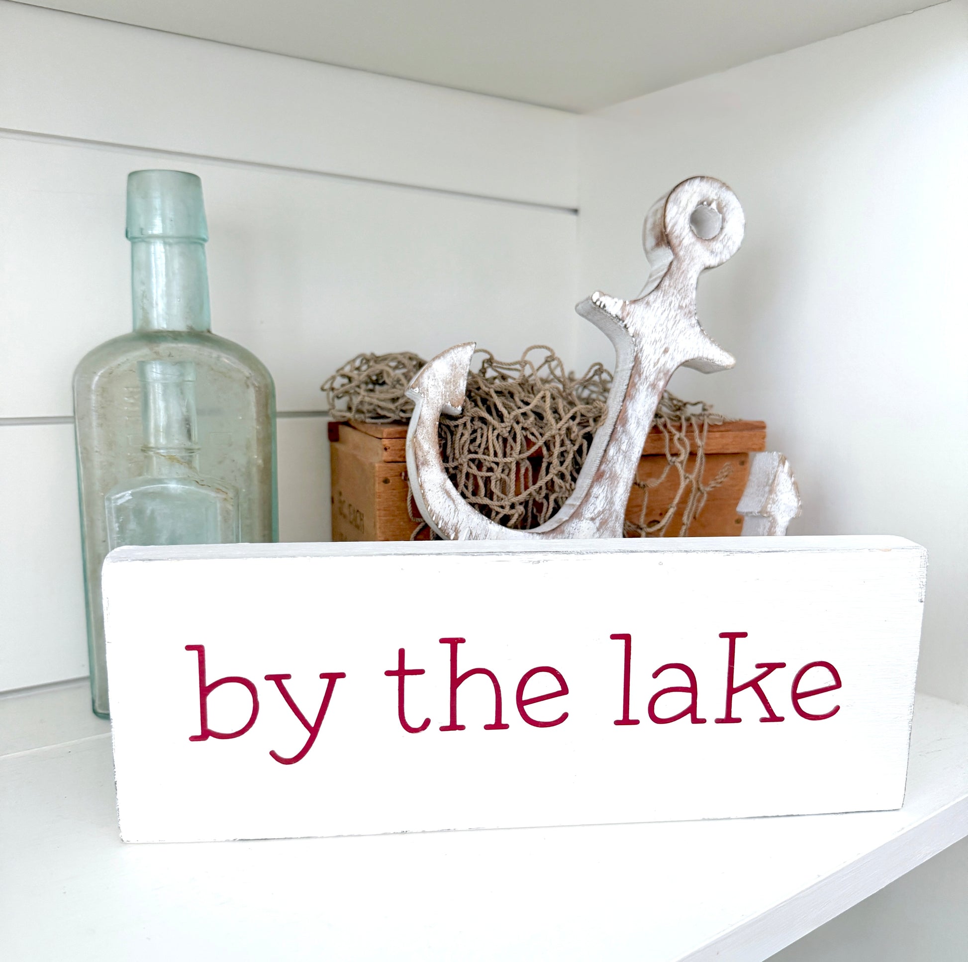 Decorative shelf with anchor, bottle, and 'by the lake' sign on a white background