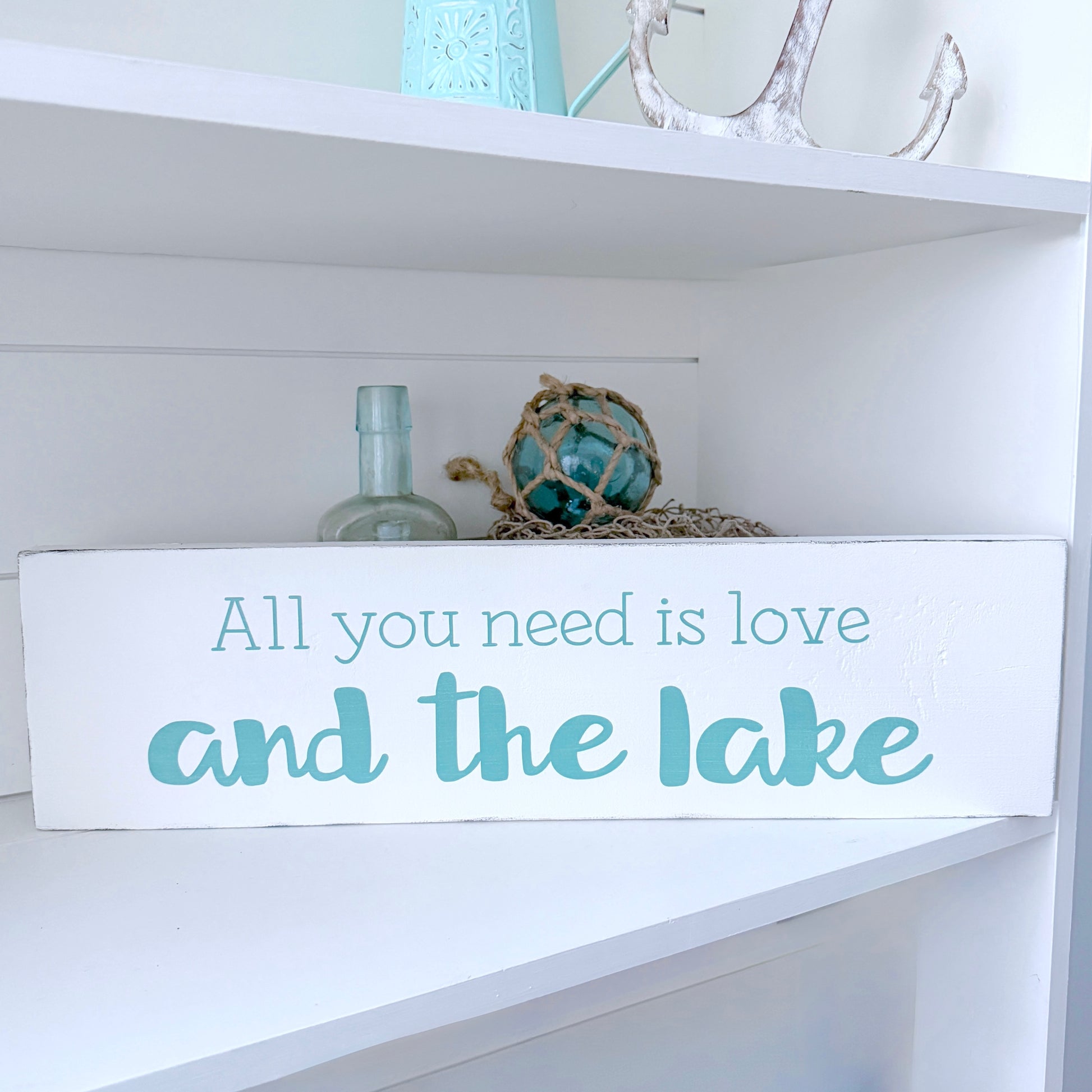 Decorative sign with 'All you need is love and the lake' text on a shelf with decorative items.