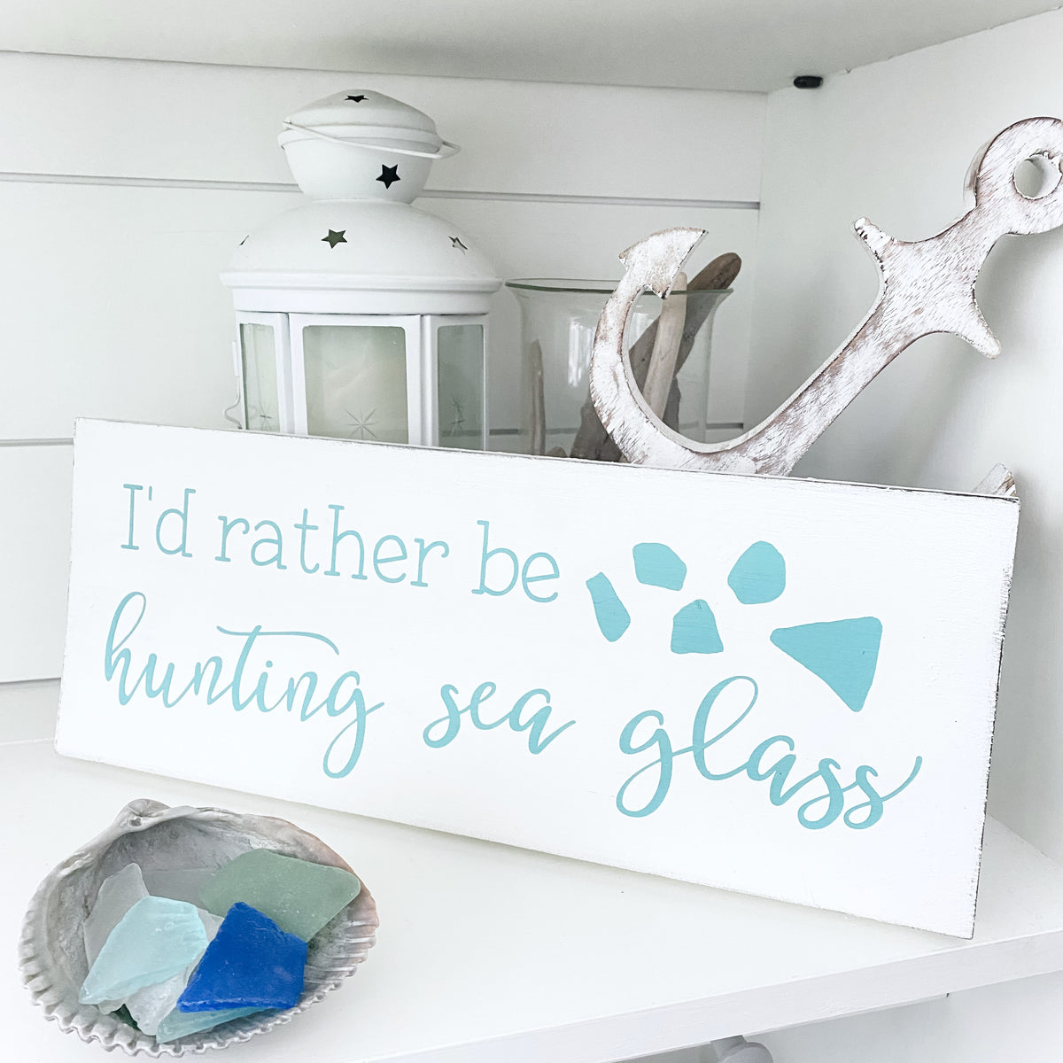 Decorative sign with 'I'd rather be hunting sea glass' text on a shelf with decorative items.