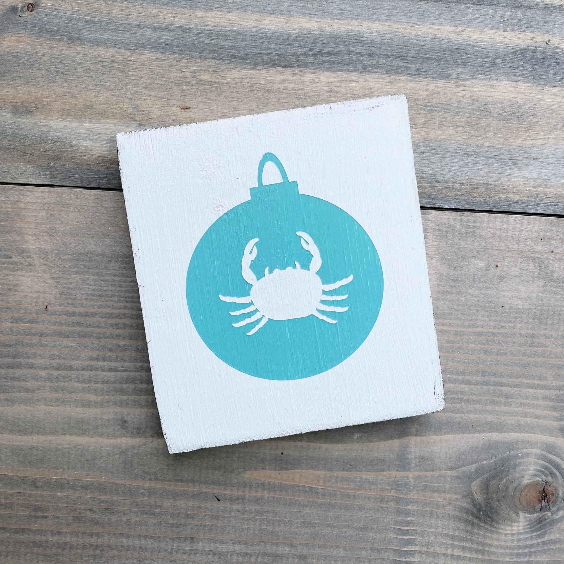 Square white card with a blue circle featuring a white crab design on a wooden surface