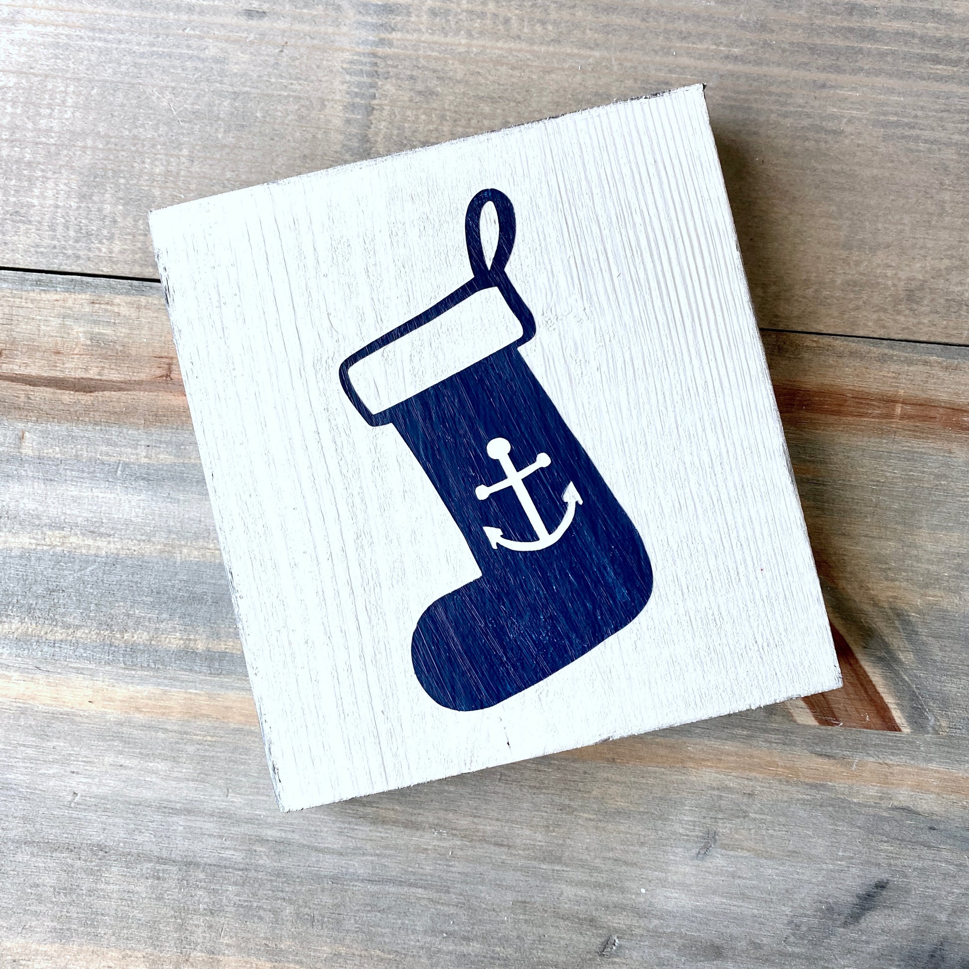 Wooden sign with a blue stocking design featuring an anchor on a wooden surface