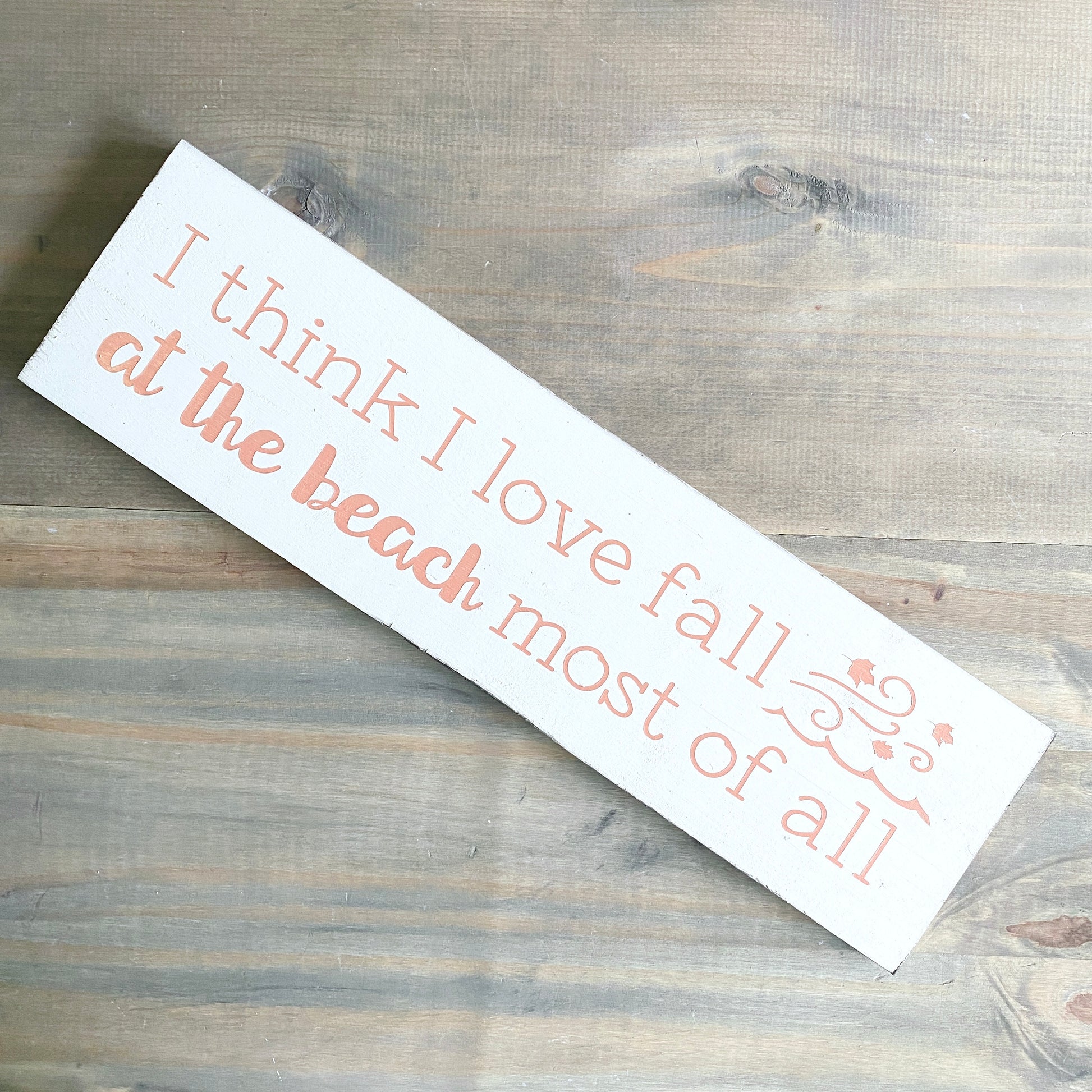 Wooden sign with text 'I think I love fall at the beach most of all' on a wooden surface