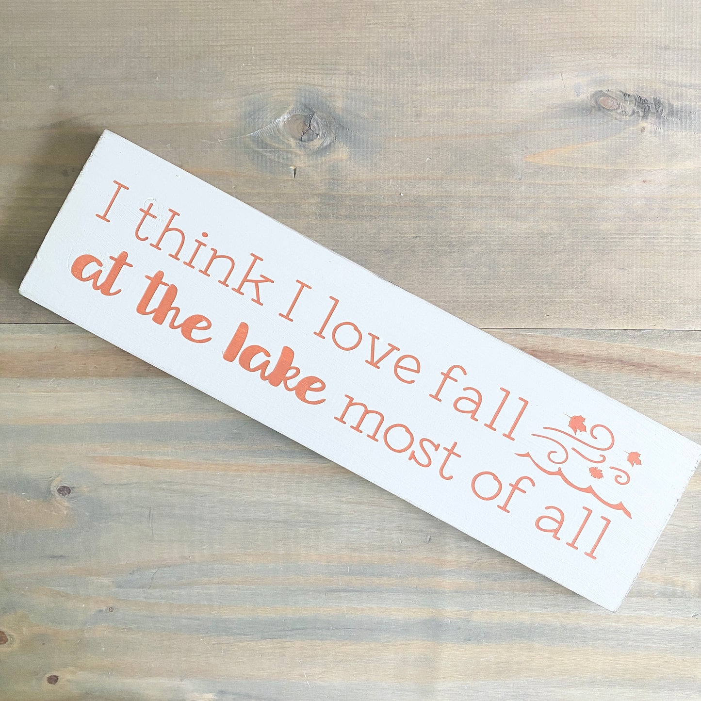 Wooden sign with text 'I think I love fall at the lake most of all' on a wooden surface