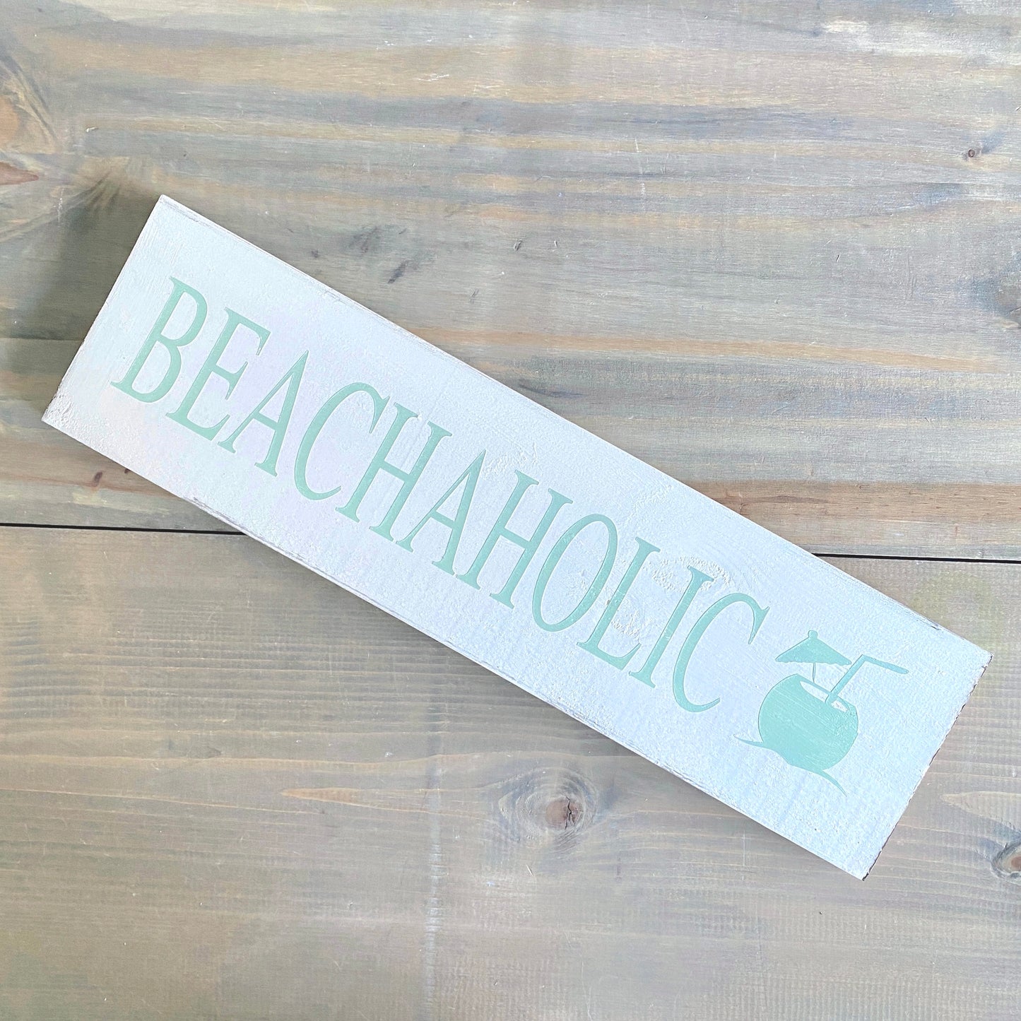 Wooden sign with 'BEACHAHOLIC' text and a beach ball graphic on a wooden surface.