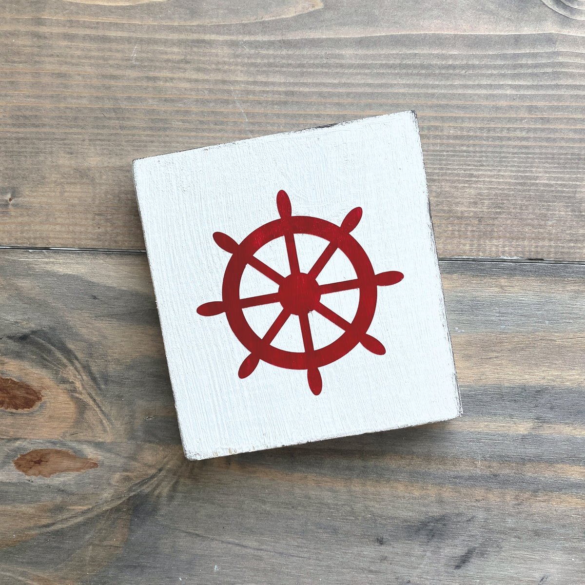 White square sign with a red ship's wheel design on a wooden surface