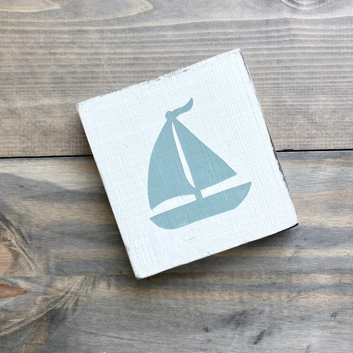 Sage green sailboat on a white background laying on a rustic wood surface