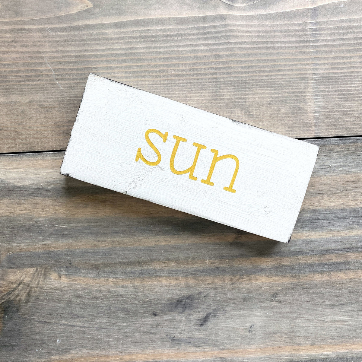 White rectangular sign with 'sun' in yellow on a wooden surface