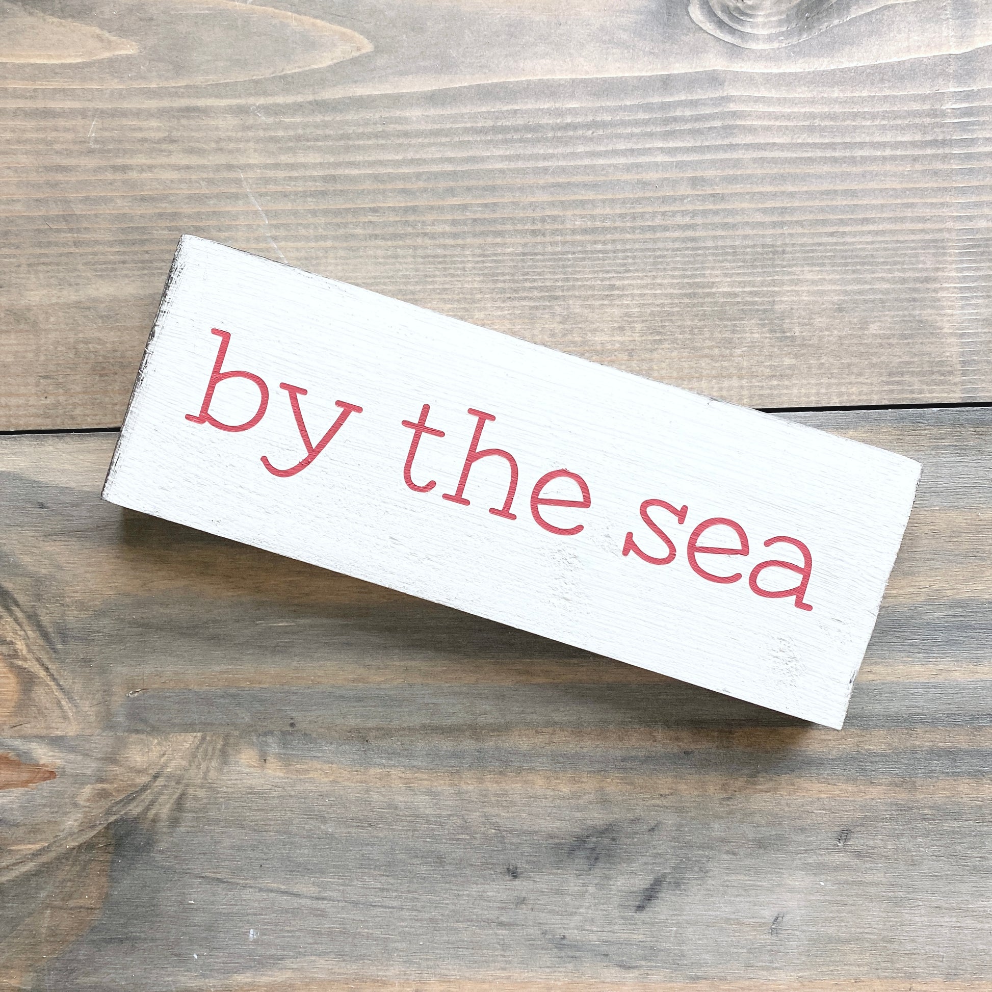 Wooden sign with 'by the sea' text on a wooden surface