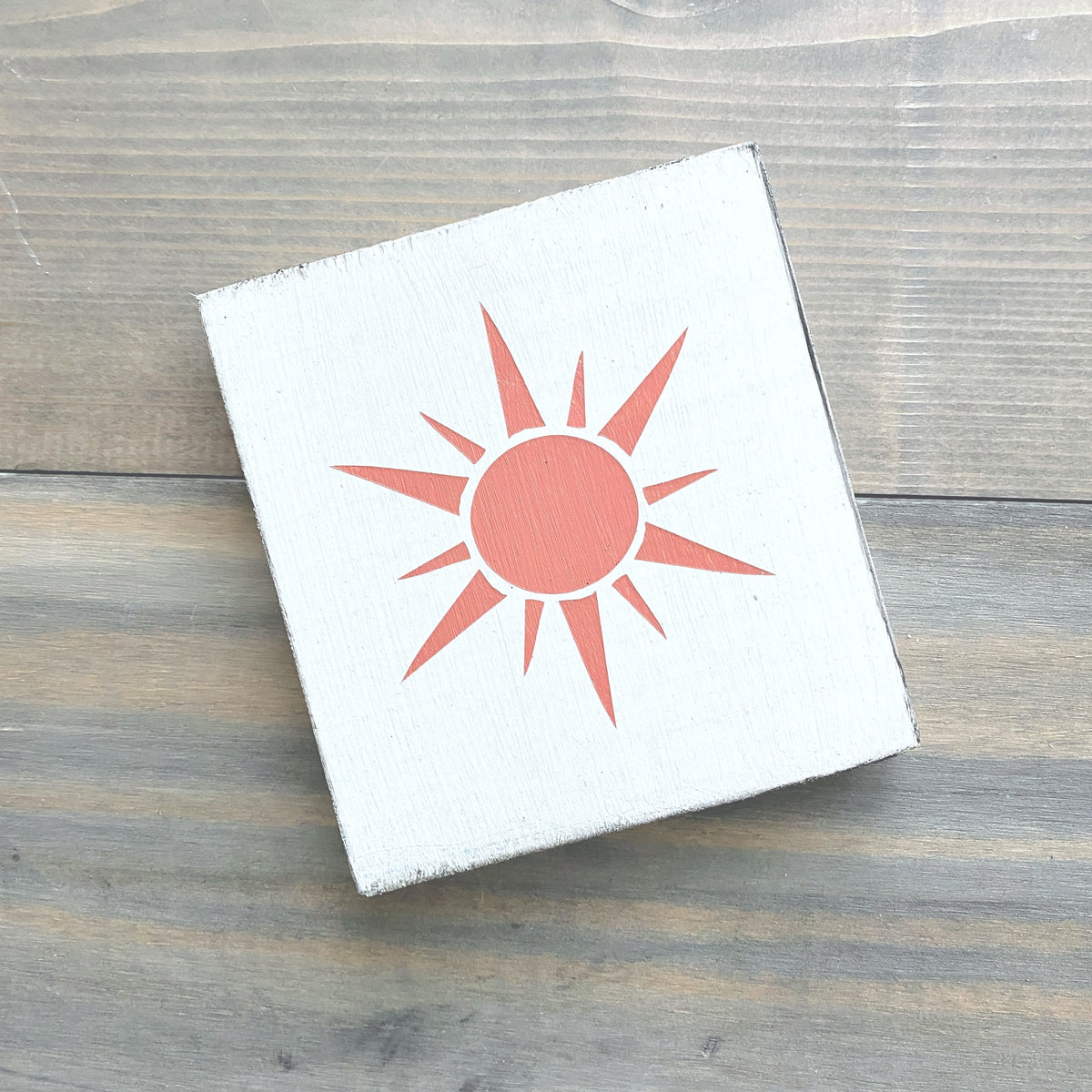 white square sign with a pale orange sunshine graphic handpainted and displayed on a wooden surface