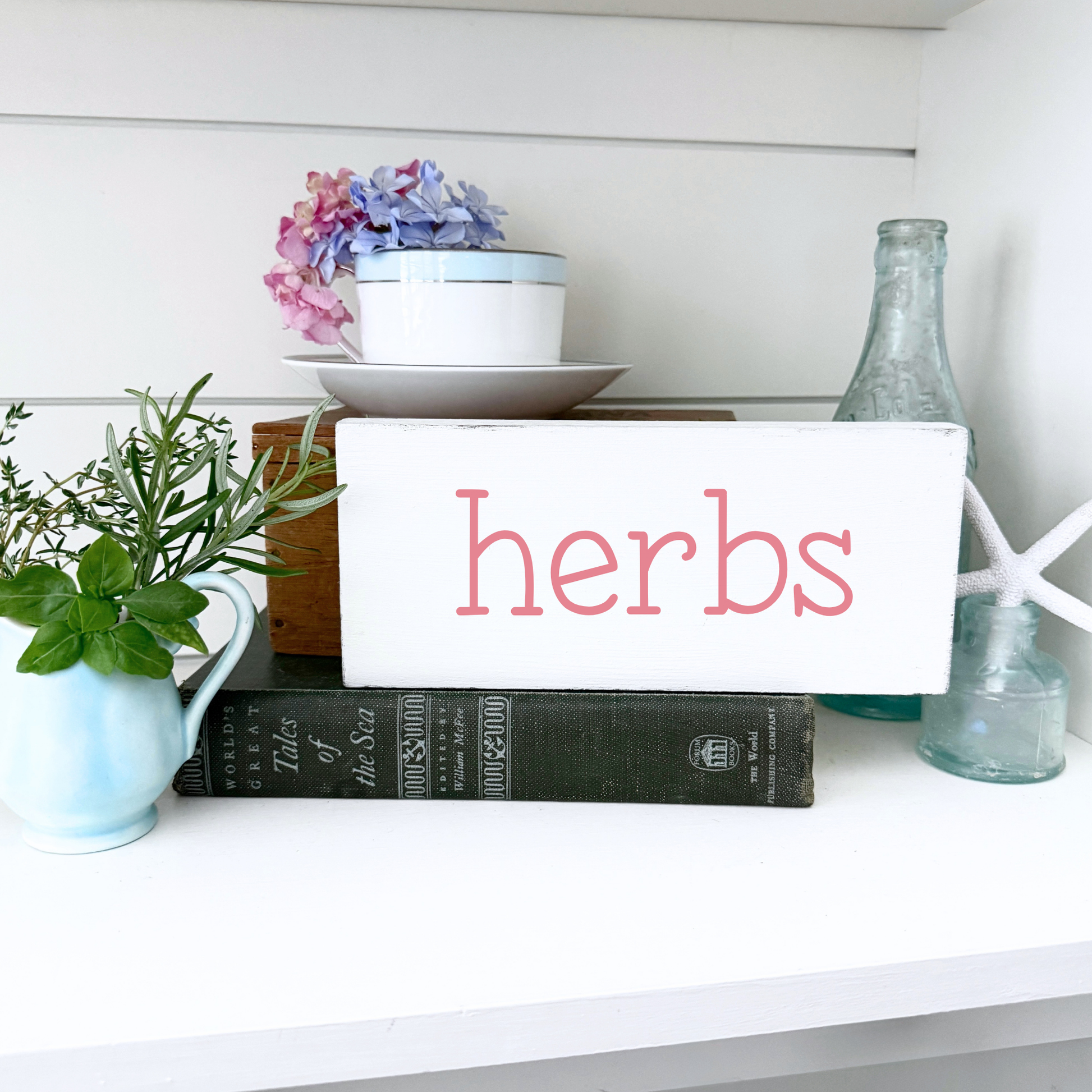 Decorative shelf with a sign labeled 'herbs', books, and plants.