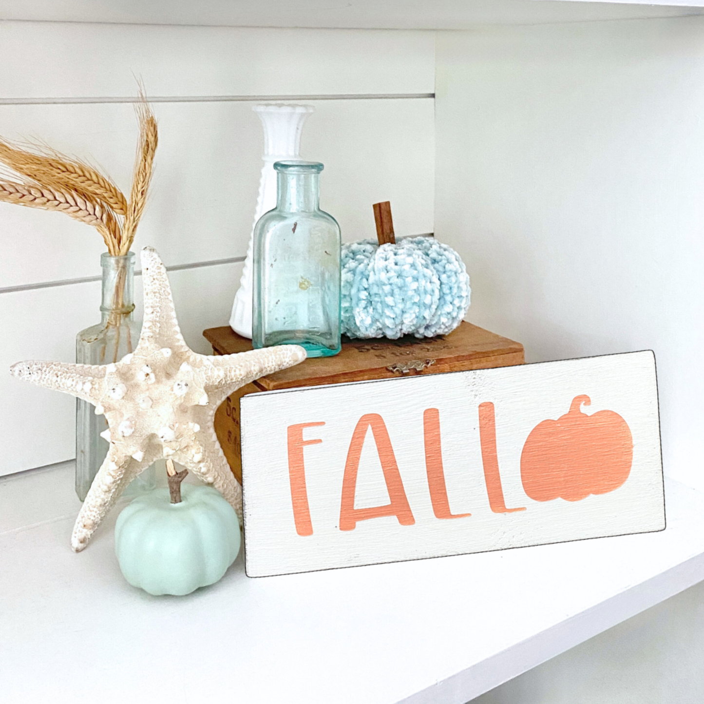 Decorative setup with 'Fall' sign, pumpkins, and starfish on a white surface.