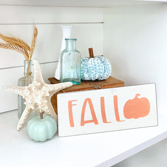 Decorative setup with 'Fall' sign, pumpkins, and starfish on a white surface.