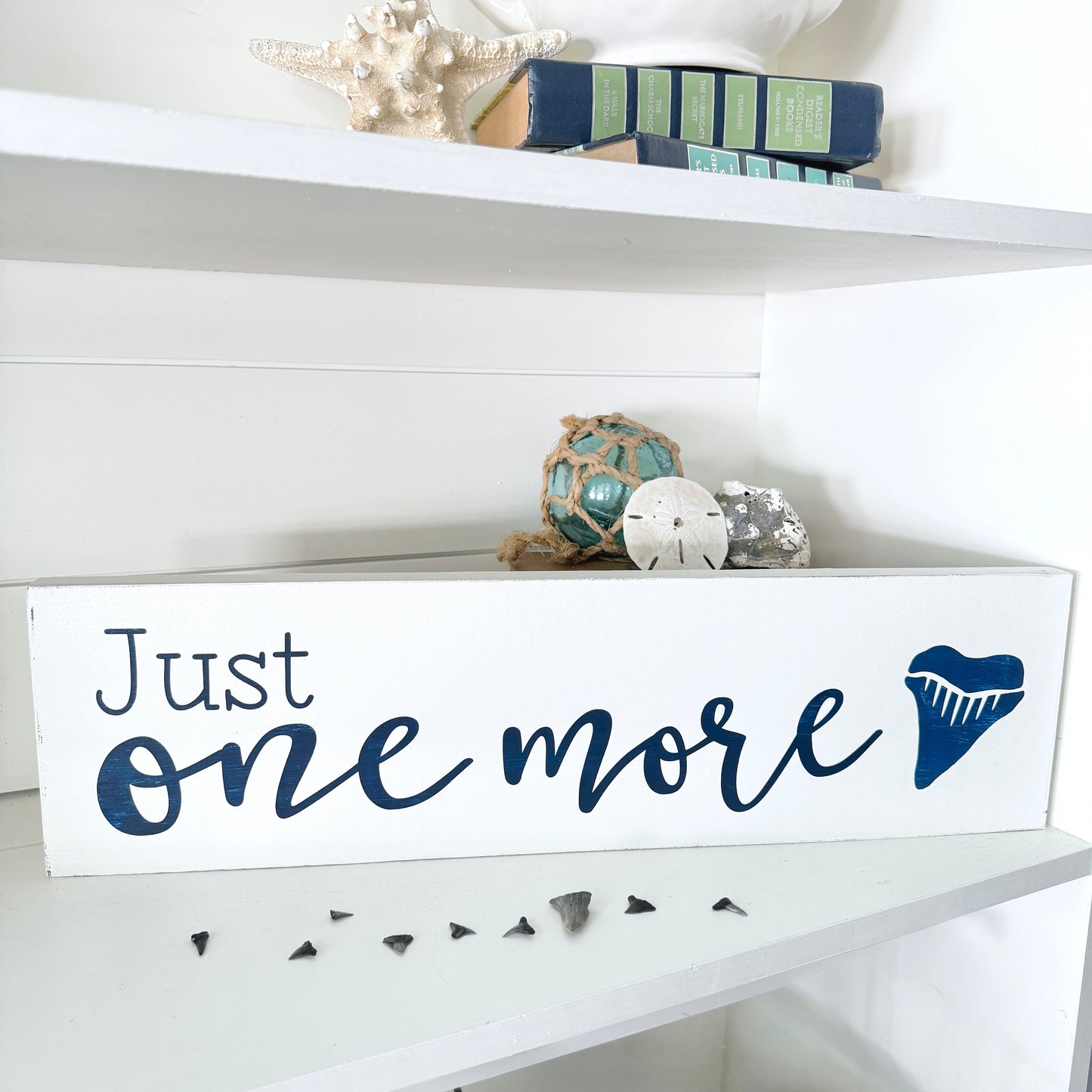 Decorative sign with 'Just one more' text on a white shelf with decorative items.