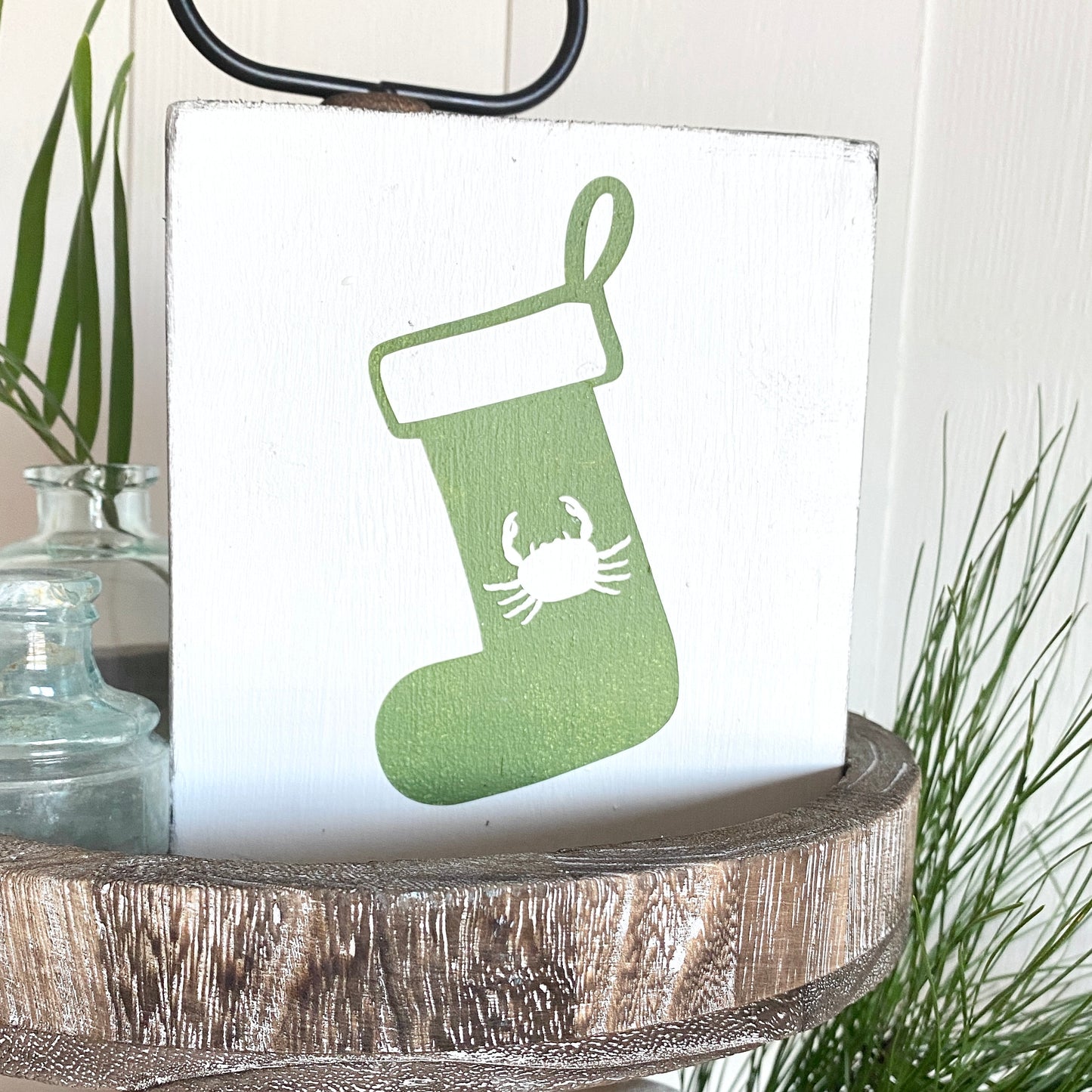 Decorative sign with green stocking and crab design on a white background, placed on a wooden surface.