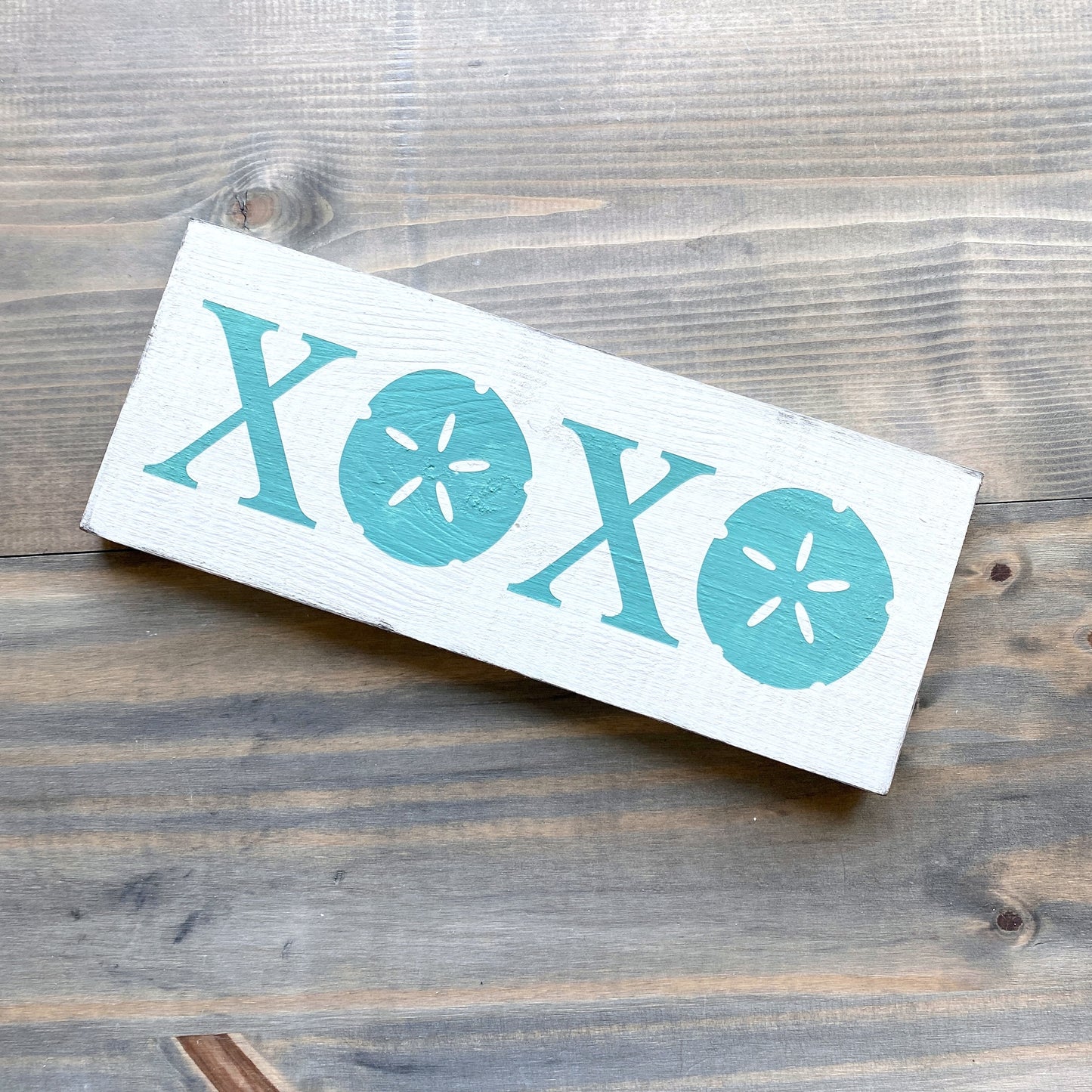 Wooden sign with 'XOXO' and sand dollar designs on a wooden surface