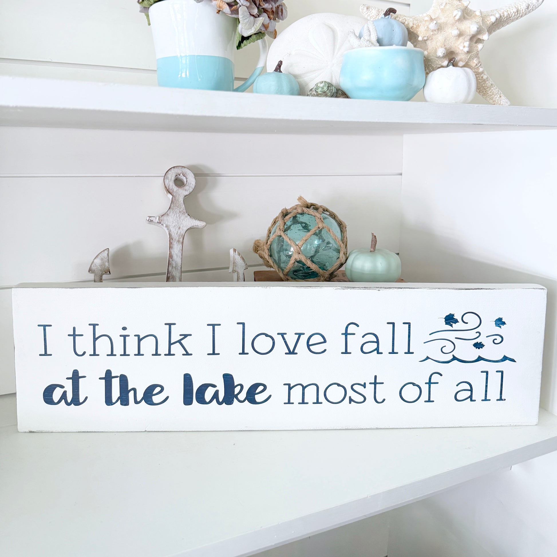Decorative sign with 'I think I love fall at the lake most of all' text on a shelf with decorative items.
