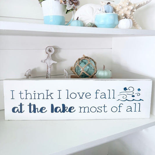Decorative sign with 'I think I love fall at the lake most of all' text on a shelf with decorative items.